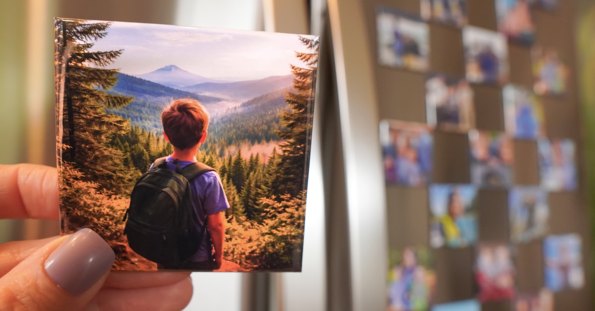 Hand holding a custom photo magnet of a boy looking at mountains on a fridge